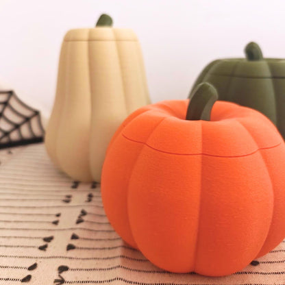 Orange round pumpkin container with lid in front, with tall desert tan and dark green pumpkin containers behind it.