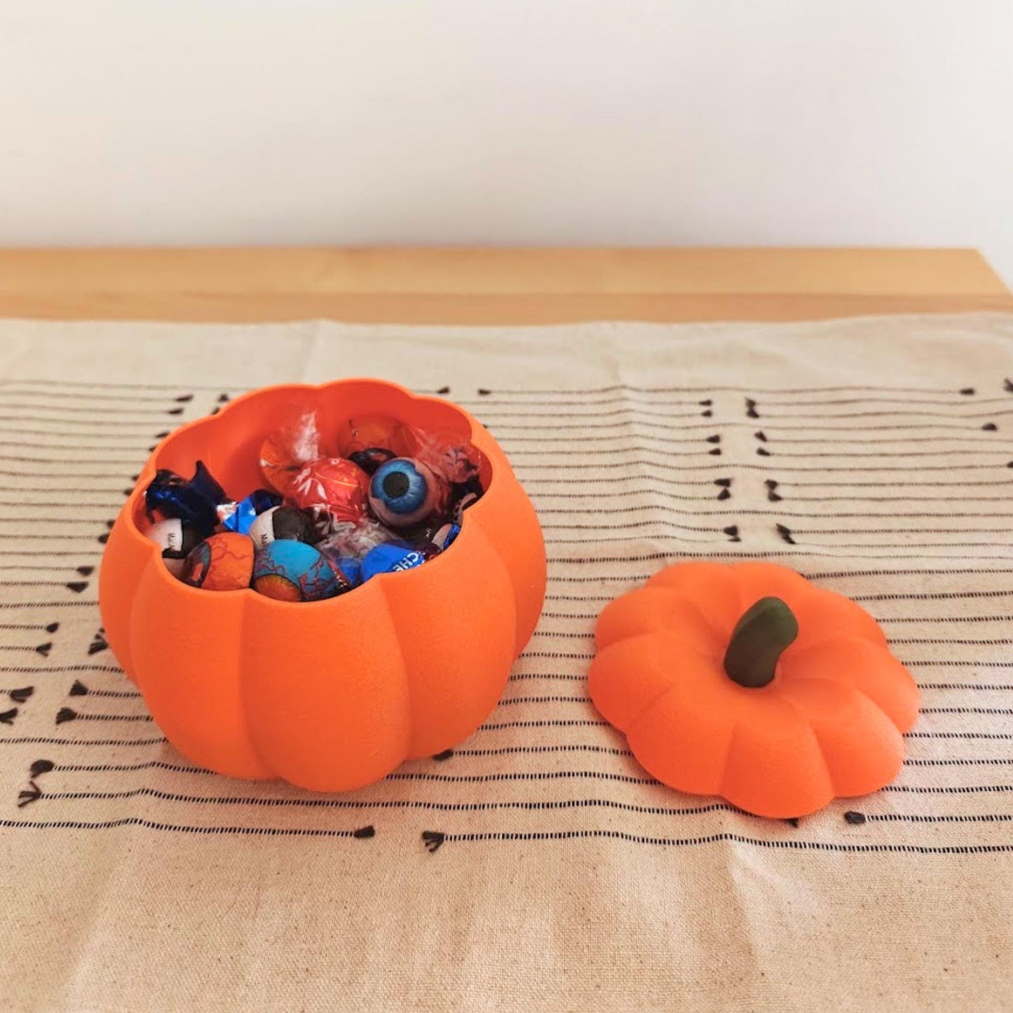 Orange pumpkin candy bowl filled with individually wrapped Halloween sweets, with the removable pumpkin lid beside it.