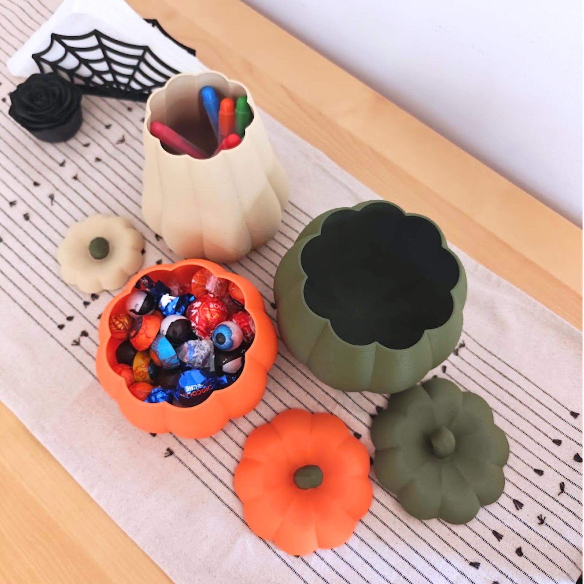 Open pumpkin containers used for storage, with the orange bowl holding wrapped candy and the tall desert tan container holding pens.