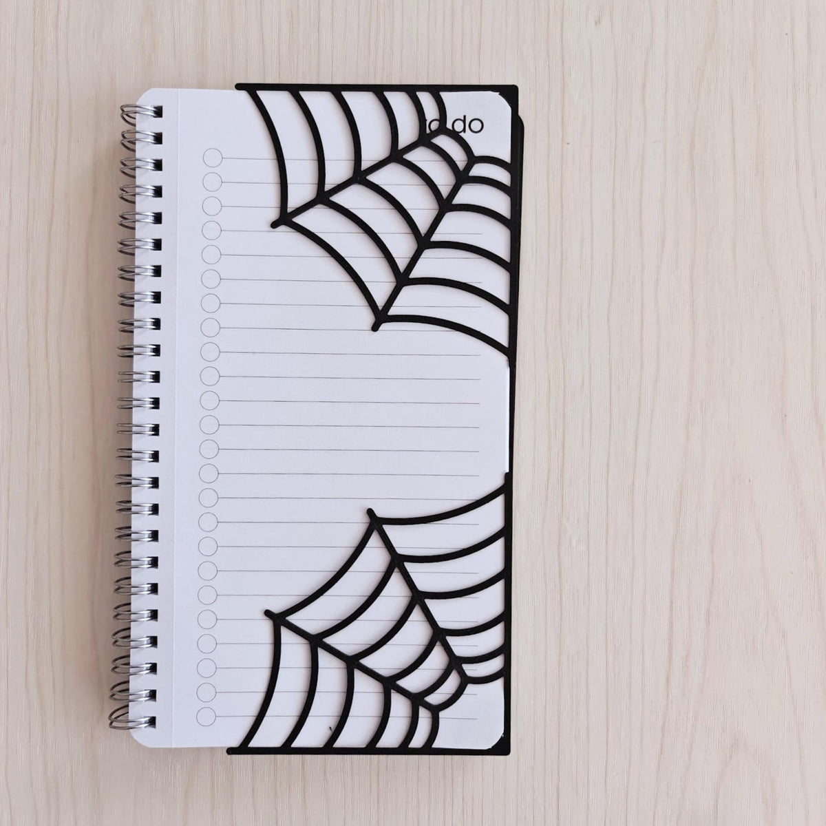 Two black spiderweb bookmarks displayed together on a white spiral notebook