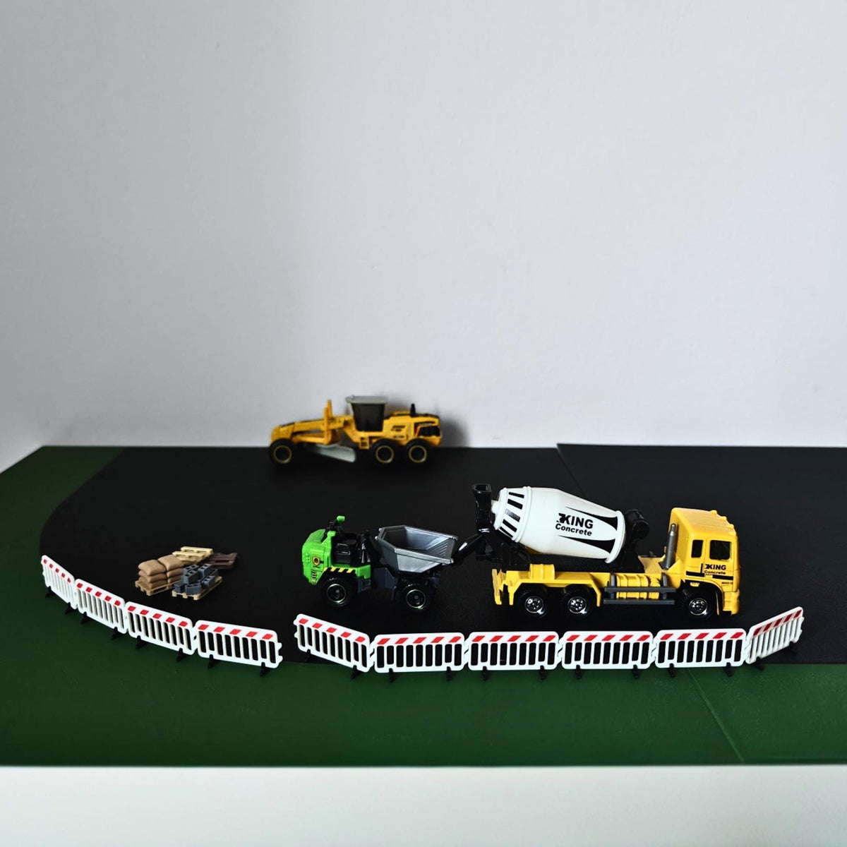 Miniature roadwork scene with connected crowd control barriers and construction vehicles