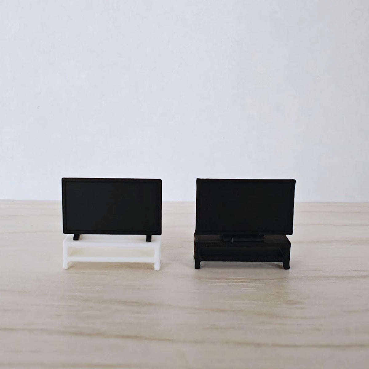 Two miniature 1:64 scale TVs displayed on black and white TV console tables