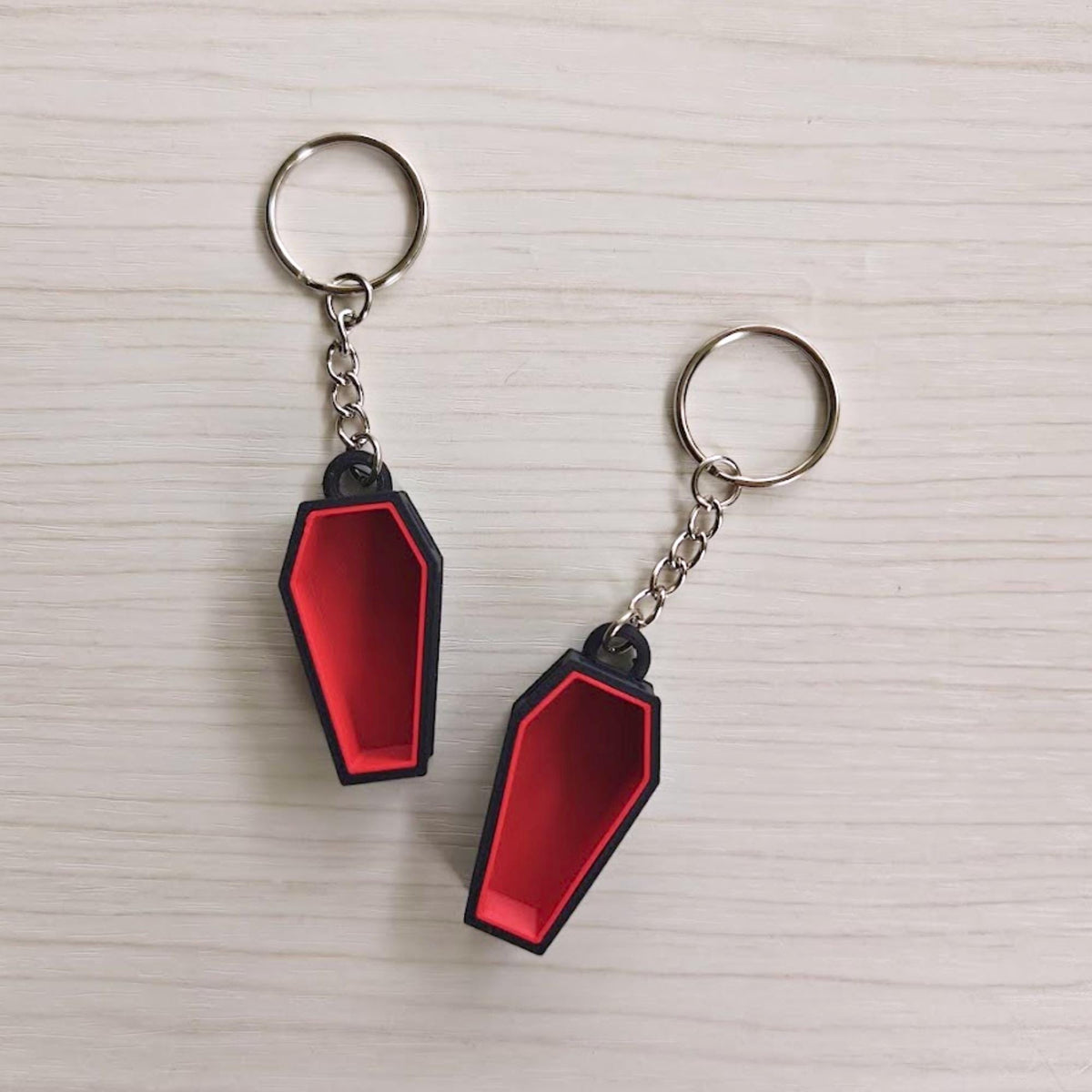 Two red and black coffin keychains shown from the front
