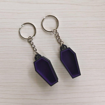 Two purple and black coffin keychains with metal key rings