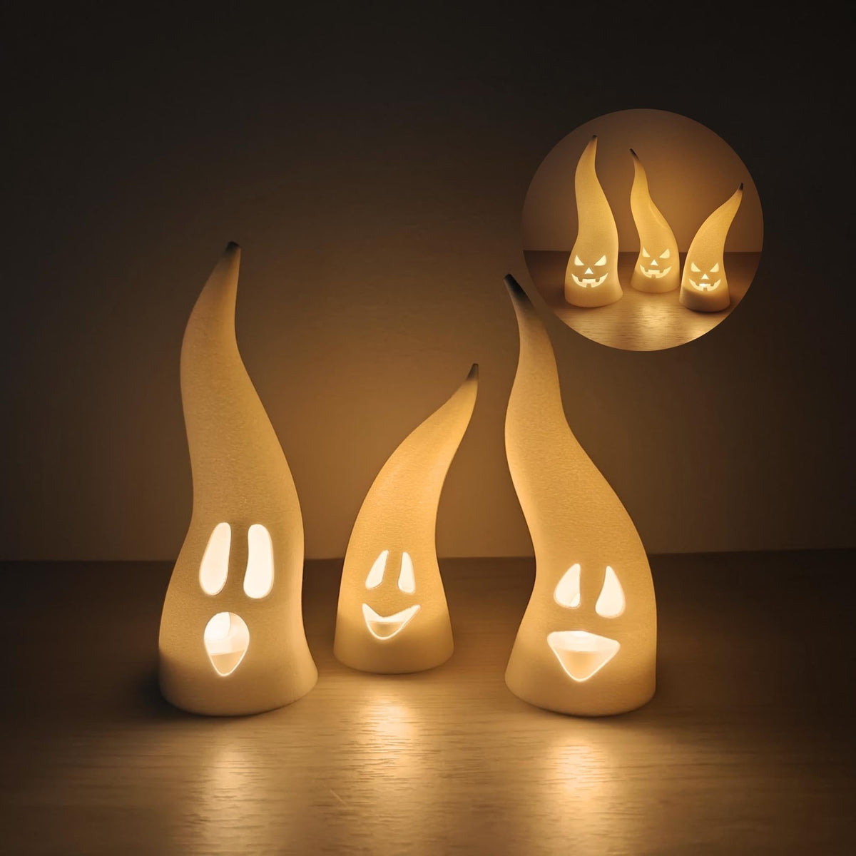 Set of three white ghost LED tealight covers with silly faces glowing warmly in a dark room.
