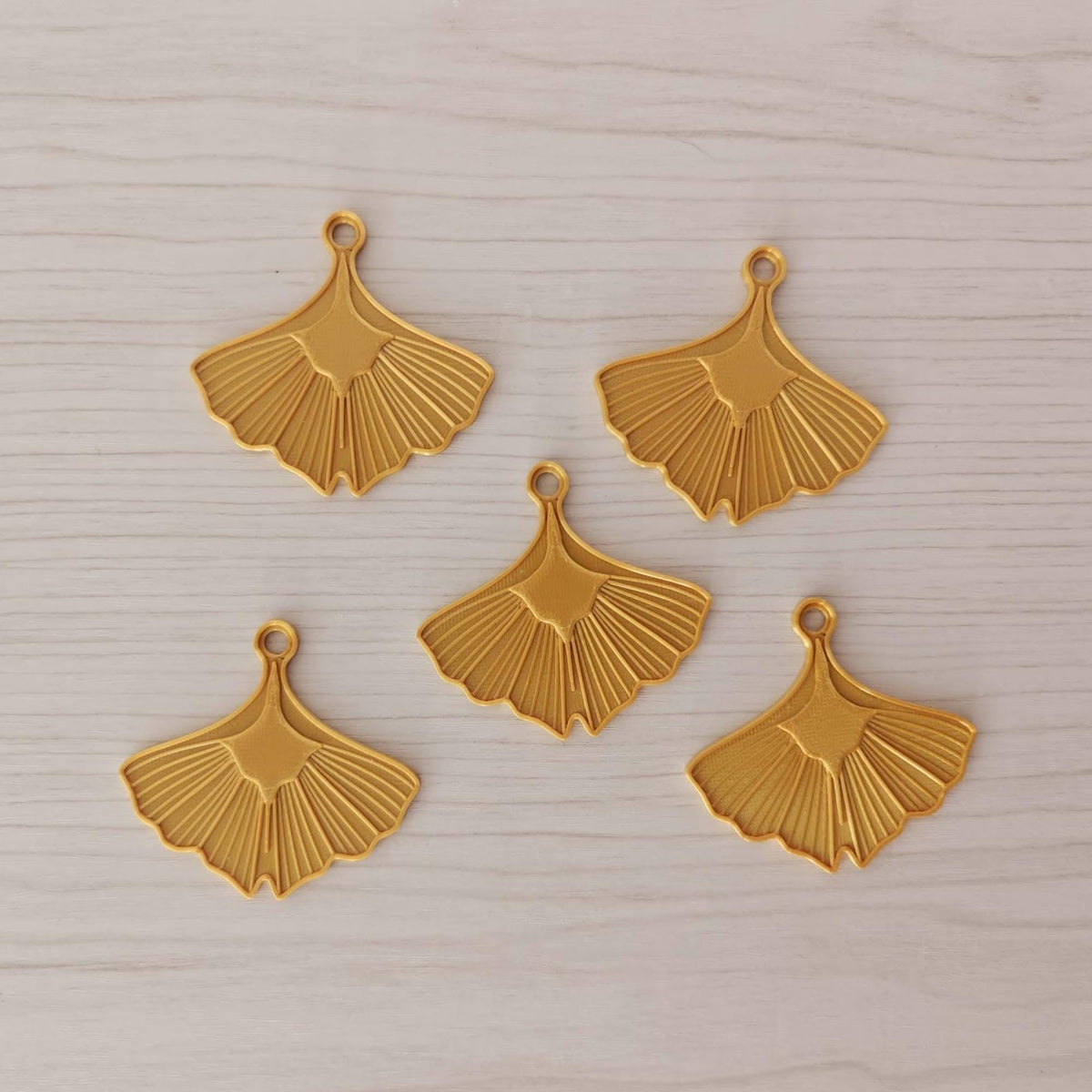 Set of five gold ginkgo leaf ornaments arranged together on a light wooden surface.
