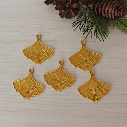 Set of five gold ginkgo leaf hanging ornaments arranged on a light wood background with evergreen branches.