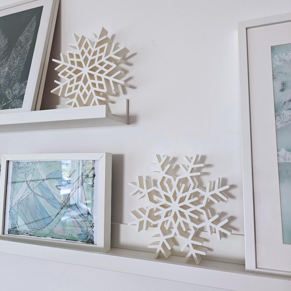 Large 3D printed snowflake decorations styled on white wall shelves with framed artwork