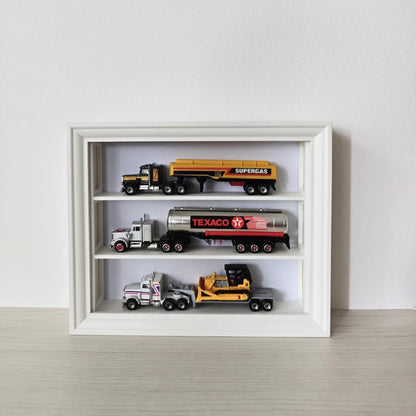 White horizontal VÄSTANHED frame insert with three shelves displaying miniature trucks and toy vehicles.