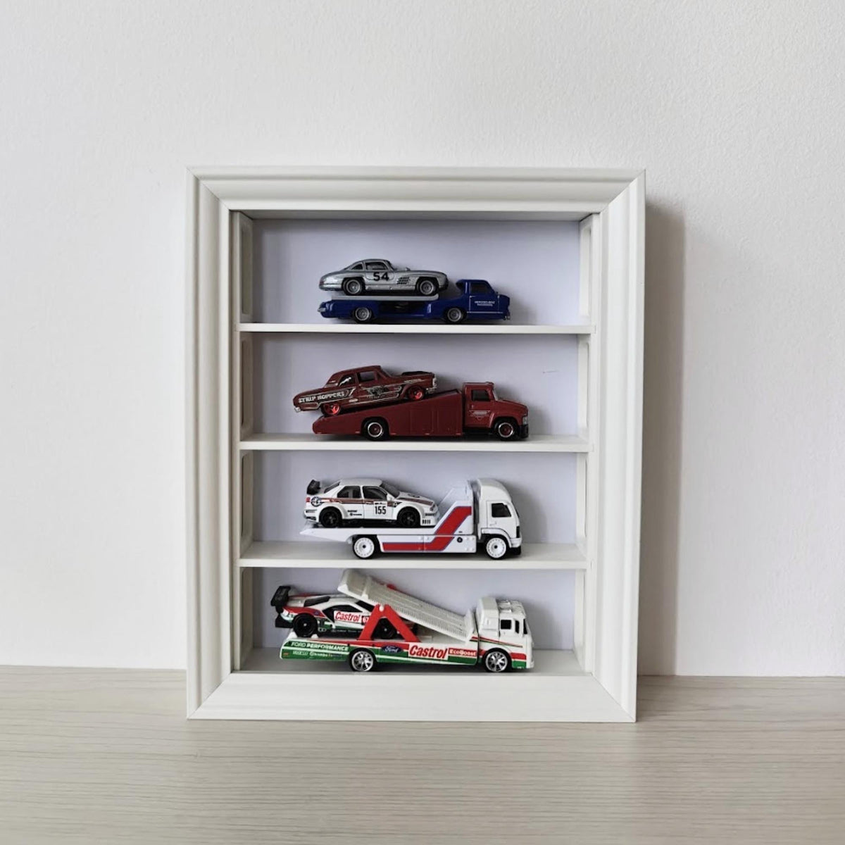 Front view of vertical white VÄSTANHED display insert with four shelves holding collectible cars.