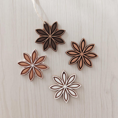 Set of star anise hanging ornaments in mixed brown, white and natural tones on a light wood background.