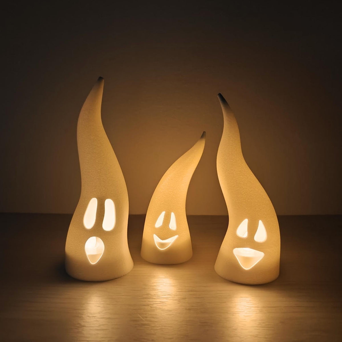 Set of three white ghost LED tealight covers with evil grinning faces illuminated from inside.